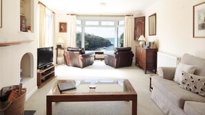 A living room with a large window, leather sofas, a coffee table, and a television. - Green Door - Upper Tregudda (Port Isaac)