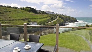 A table with chairs and a view of a coastal landscape with houses on a hill and the ocean. - Green Door - Upper Tregudda (Port Isaac)
