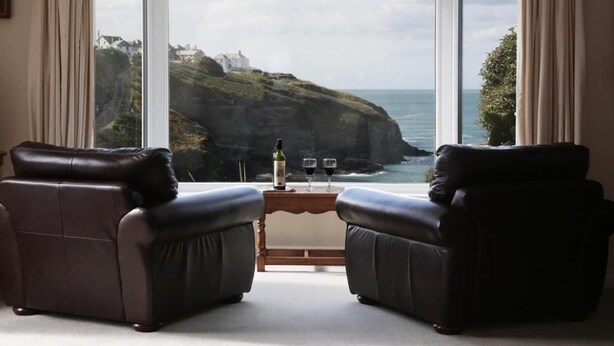 A room with two leather armchairs facing a large window overlooking a coastal landscape. - Green Door - Upper Tregudda (Port Isaac)
