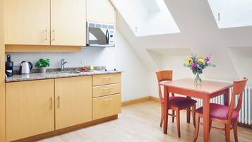 Una cocina moderna con armarios de madera, un microondas y un lavabo. Hay una mesa de comedor con sillas y un florero. La habitación tiene un techo inclinado con tragaluces.