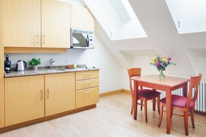 Una cucina moderna con mobili in legno, un forno a microonde e un lavandino. È presente un tavolo da pranzo con sedie e un vaso di fiori. La stanza ha un soffitto a sbalzo con lucernari.
