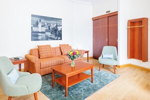 Uma sala de estar com um sofá, duas poltronas, uma mesa de centro e um quadro de uma paisagem urbana.