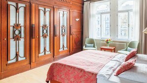 A hotel room with a large bed, a wooden wardrobe with glass doors, a window with a view of buildings, and a chair by the window. - Hapimag Resort Prague (Prague)