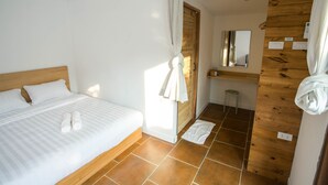 Habitación de hotel con una cama de cabecera de madera, un baño con pared de madera y un espejo, y un taburete pequeño.