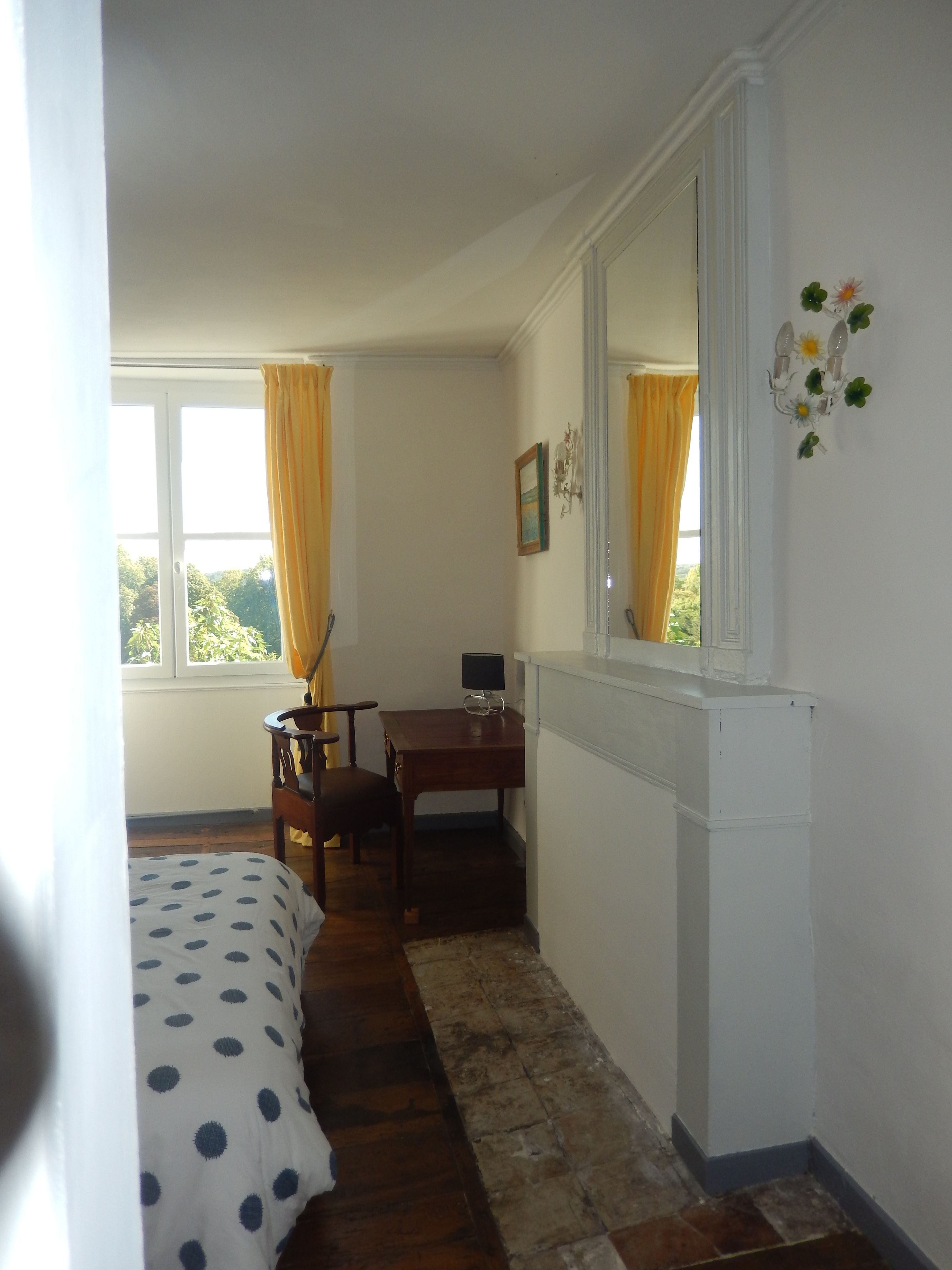 A bedroom with a bed, a desk, a chair, a mirror, and a window with curtains.