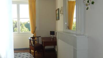 A bedroom with a bed, a desk, a chair, a mirror, and a window with curtains.