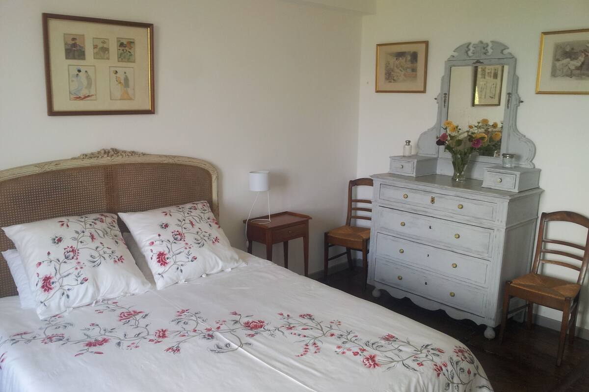 Une chambre à coucher avec un lit, une commode, des chaises et des tableaux encadrés accrochés au mur.