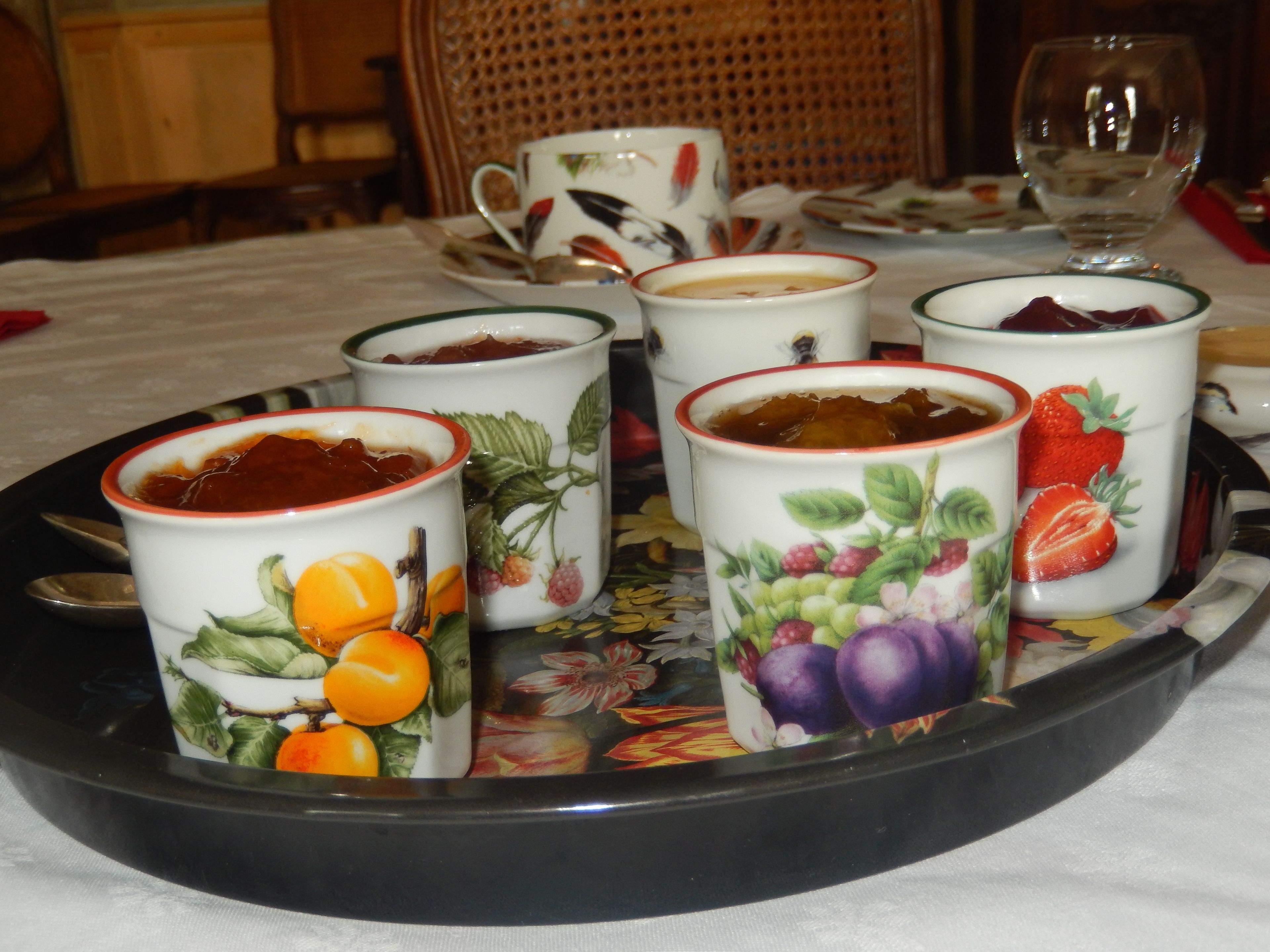 A tray with several fruit-themed cups and saucers, a glass of water, and a wicker chair in the background.