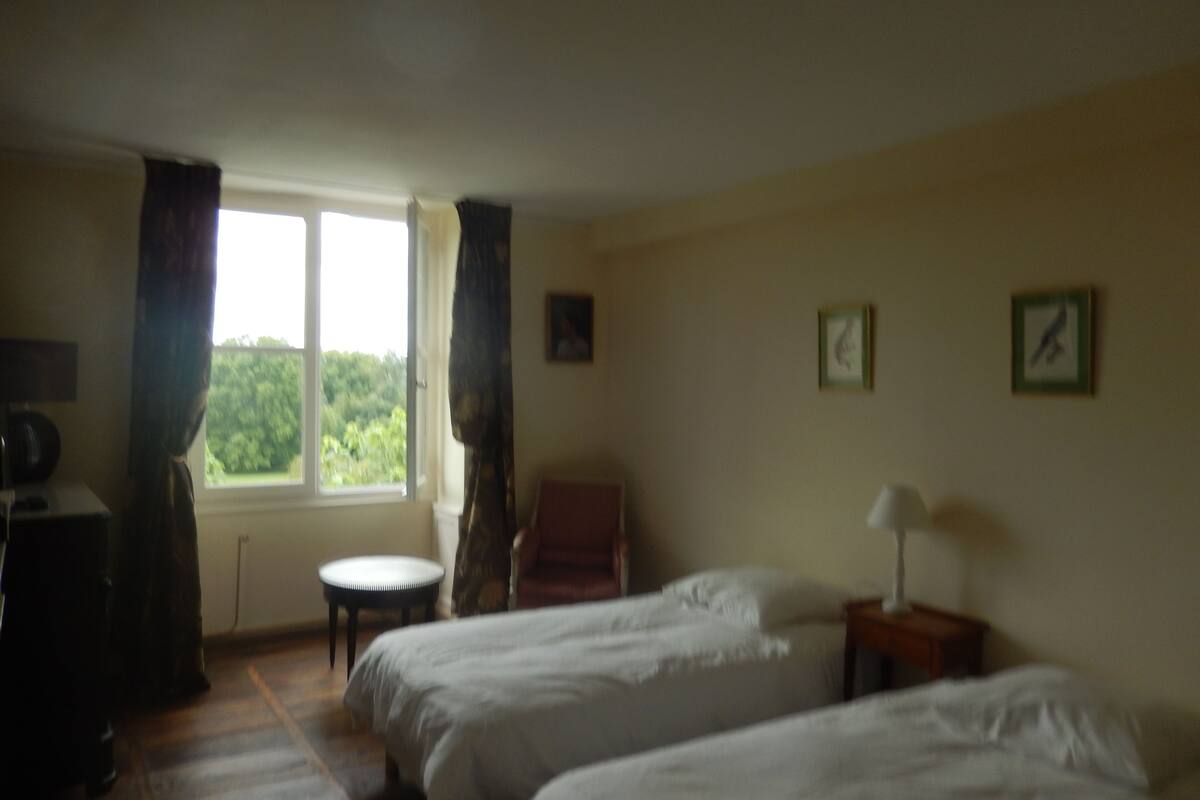 Une chambre avec deux lits, une chaise, une petite table et une fenêtre avec des rideaux.