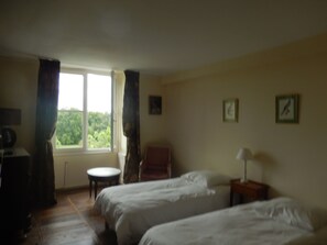 Ein Zimmer mit zwei Betten, einem Sessel, einem kleinen Tisch und einem Fenster mit Vorhängen.