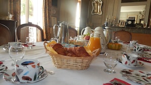 Une table mise pour le petit-déjeuner, avec des croissants, du jus d’orange et du café, dans un coin repas agrémenté de chaises et d’une table.