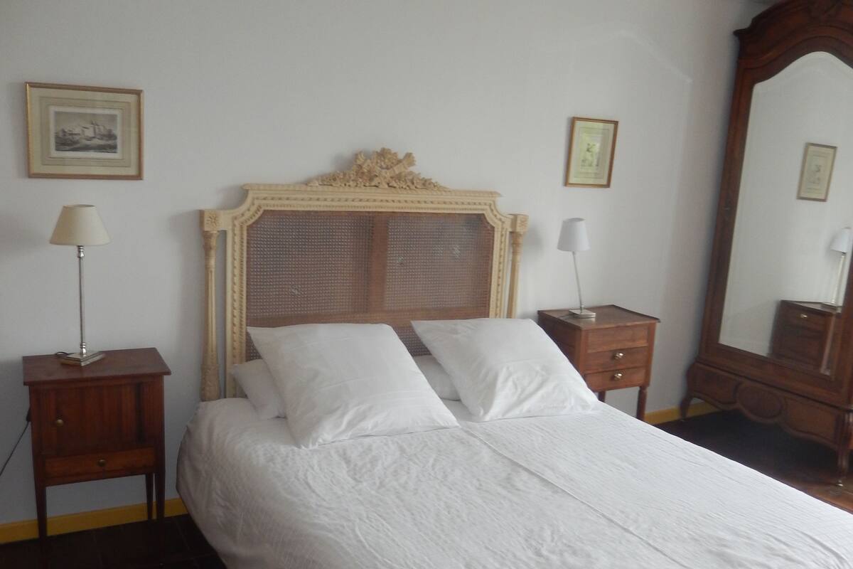 Une chambre à coucher avec un grand lit, une tête de lit en bois, deux tables de chevet avec des lampes, une commode et un miroir.