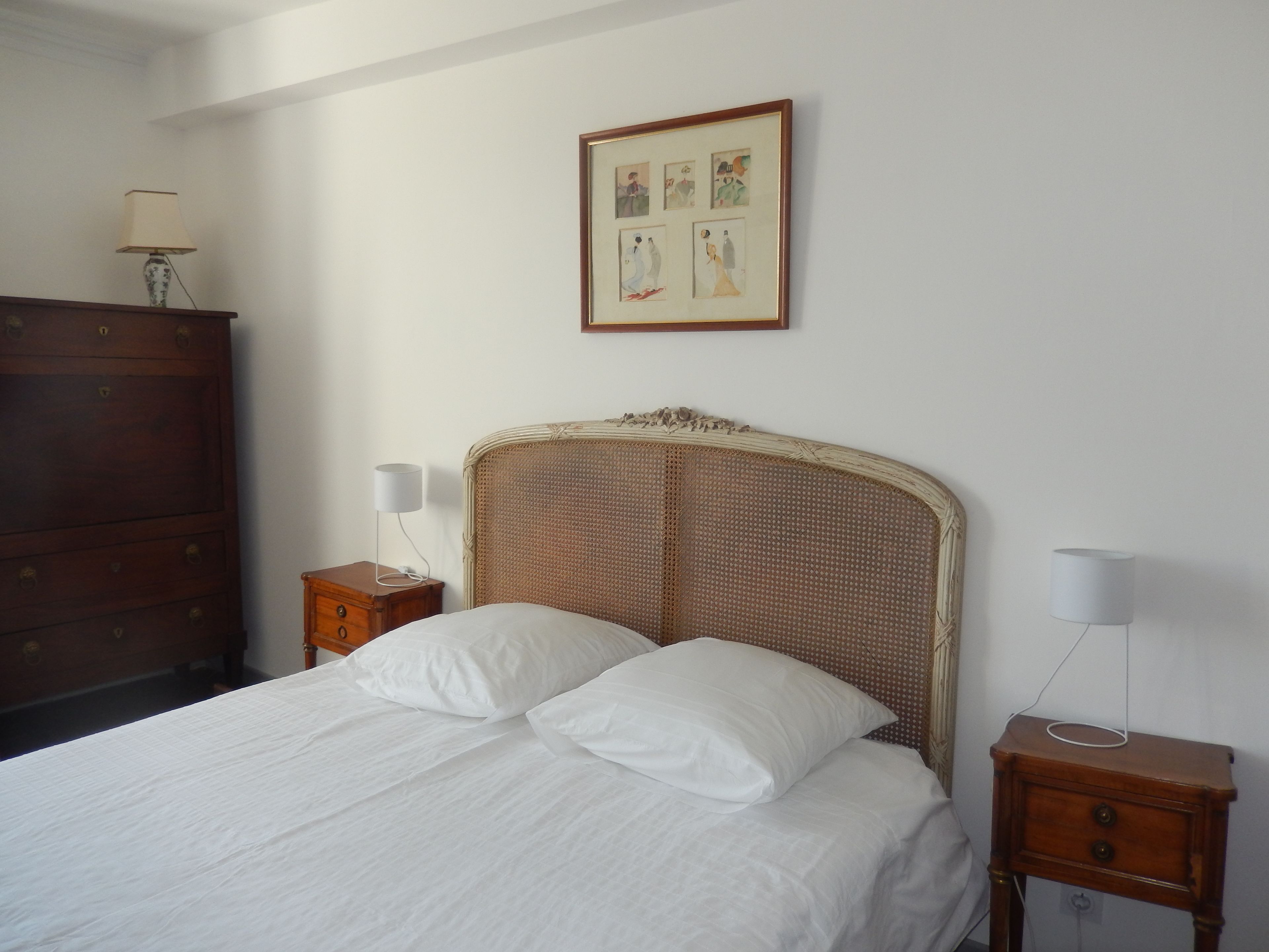 A bedroom with a bed, two bedside tables, a dresser, and a framed picture on the wall.