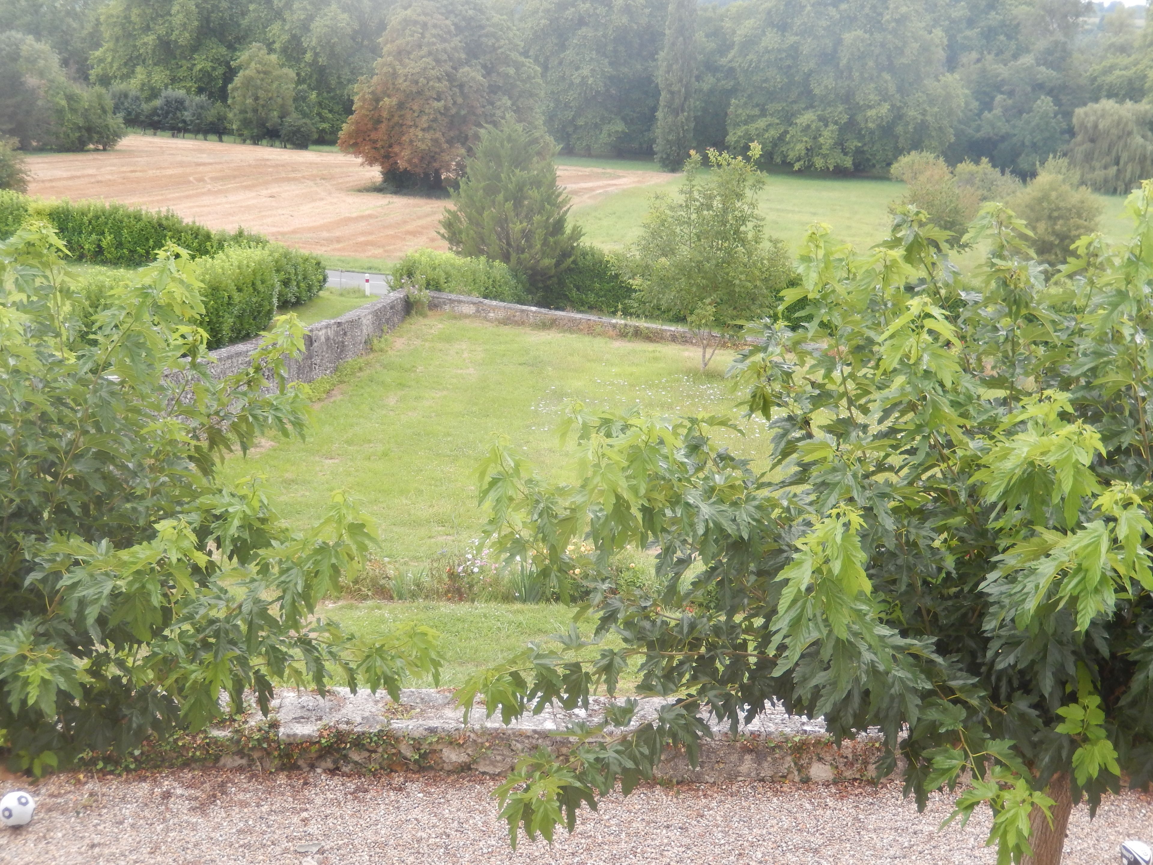 Un jardin avec un mur de pierre, une pelouse et divers arbres.