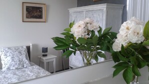 Une chambre à coucher avec un lit, une table de chevet, une lampe et un miroir qui reflète des fleurs.