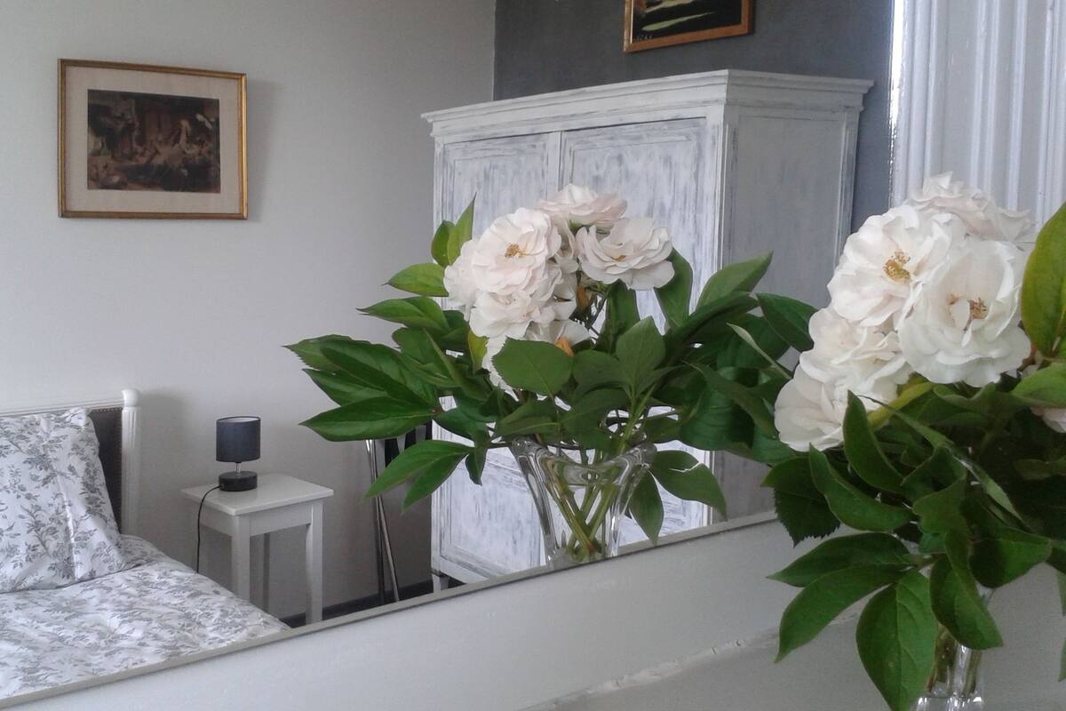 Une chambre à coucher avec un lit, une table de chevet, une lampe et un miroir qui reflète des fleurs.