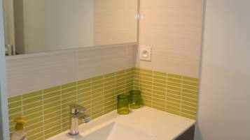 A bathroom with a white sink, green-tiled walls, a mirror, and a light fixture above the mirror.