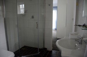 A bathroom with a glass shower enclosure, a white sink, and a mirror. - Touch of Class Villas (Pretoria)