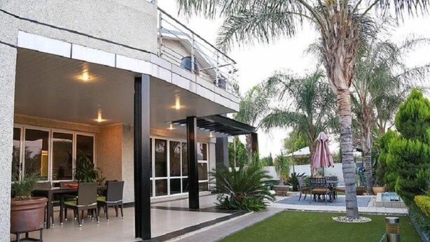 A modern building with a covered patio area, outdoor seating, and a well-maintained garden with palm trees. - Cycad Palm Boutique Guest House (Gaborone)