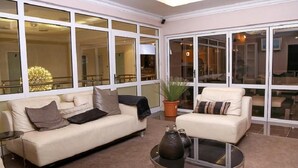 A modern living room with a beige sofa, a round coffee table, and a potted plant. - Cycad Palm Boutique Guest House (Gaborone)