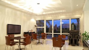 A modern dining area with a large table and chairs, a flat-screen TV, and a massage chair. - Cycad Palm Boutique Guest House (Gaborone)