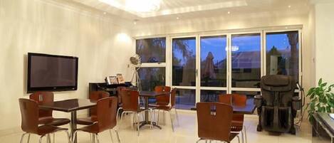 A modern dining area with a large table and chairs, a flat-screen TV, and a massage chair.