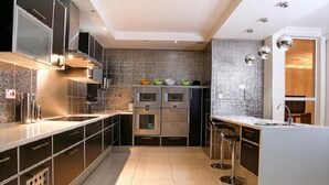 A modern kitchen with stainless steel appliances, a central island with stools, and a tiled backsplash. - Cycad Palm Boutique Guest House (Gaborone)