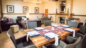 Un comedor con una mesa de madera dispuesta para seis personas, rodeada de sillas de mimbre, un sofá de cuero y una chimenea.