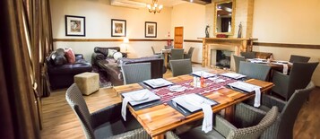 Uma sala de jantar com uma mesa de madeira preparada para seis pessoas, rodeada por cadeiras de vime, um sofá de couro e uma lareira.