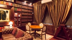 Una sala de biblioteca con estanterías, un cuadro enmarcado, un sofá de cuero y una mesa redonda con sillas.