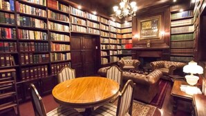 Una biblioteca con estanterías de madera, una mesa redonda de madera, sillones de cuero y una chimenea.