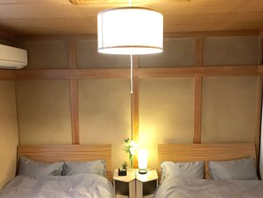 A hotel room with two beds, a nightstand with a lamp, and an air conditioning unit on the wall.