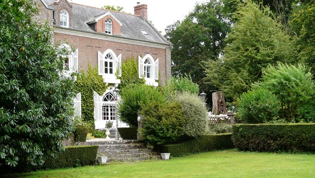 Une grande maison en briques, dotée d’une pelouse et d’un jardin bien entretenus.