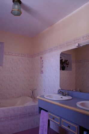Une salle de bain avec une baignoire, deux lavabos, un miroir et un porte-serviettes.
