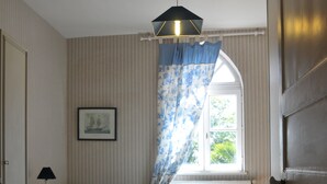 Une chambre à coucher avec un lit, une table de chevet, une lampe, une fenêtre avec des rideaux et un tableau au mur.