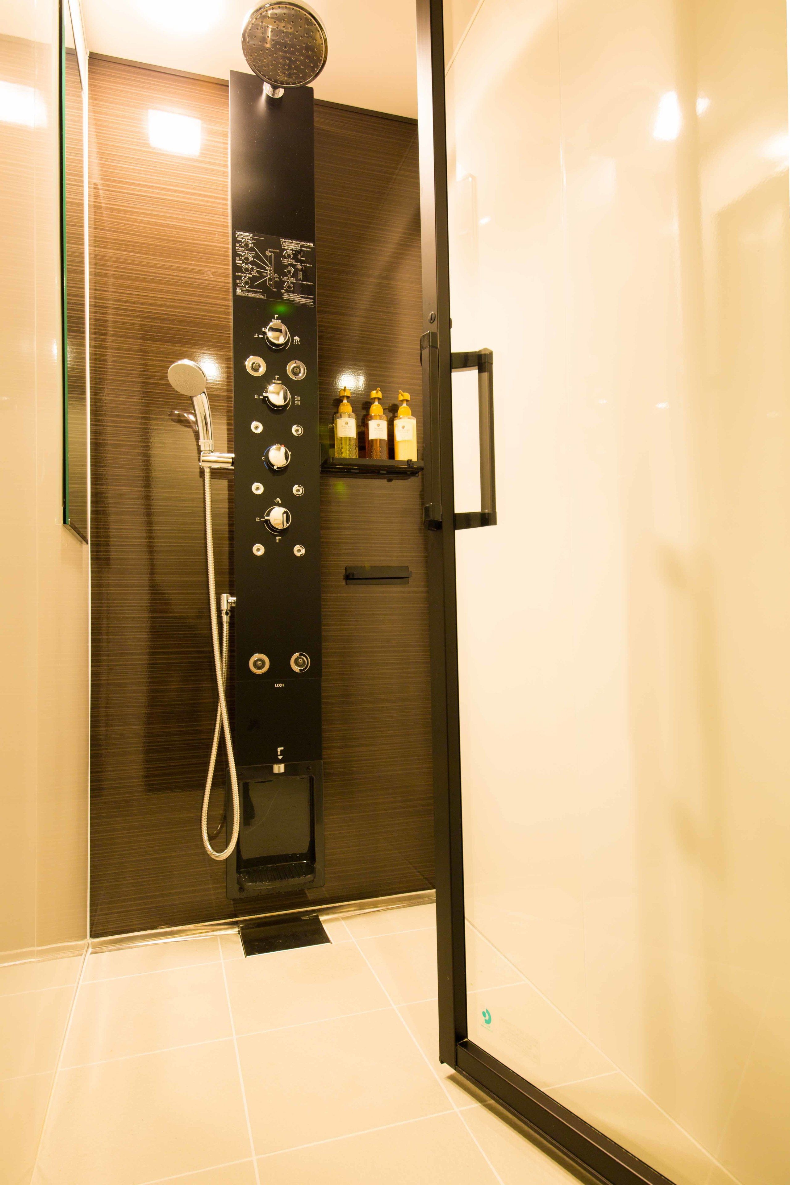 Une cabine de douche moderne dotée d’un panneau de commande, d’un pommeau de douche à main et d’une porte en verre.