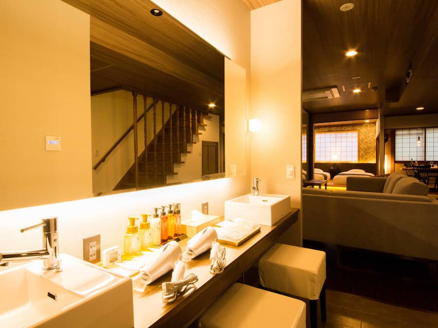 A hotel bathroom with two sinks, a mirror, and a seating area with chairs.