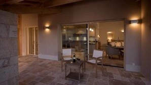 Een terras met stenen vloer, een tafel en stoelen, een glazen deur naar een keuken en een houten plafond.