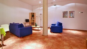 Un salón espacioso con dos sofás azules, una silla blanca, una mesita y una estantería.