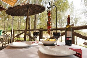 An outdoor dining area with a table set for two, a bottle of wine, a plate of food, and a hanging meat skewer. - Casa Rural Casas De Las Regatas (Castuera)