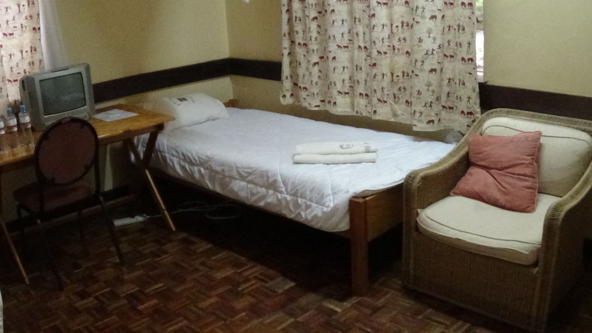 A small room with a bed, a desk with a computer, a chair, and a window with curtains.