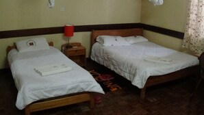 Two single beds with white linens, a wooden headboard, a nightstand with a red lamp, and a patterned rug on the floor. - Kolping Guest House (Nairobi)