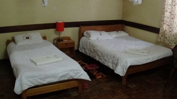 Two single beds with white linens, a wooden headboard, a nightstand with a red lamp, and a patterned rug on the floor.