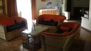 A room with wicker furniture, a glass coffee table, and a table with a white tablecloth. - Kolping Guest House (Nairobi)