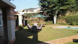 Um quintal com piscina, mesa de canto coberta e gramado.