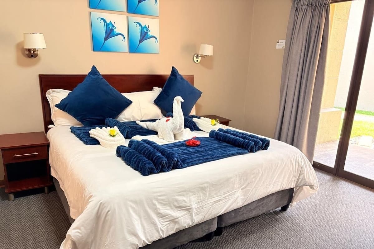 A neatly made bed with blue and white bedding, a wooden headboard, and a nightstand with a lamp.