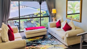 A living room with a large window, a chandelier, two sofas with red cushions, and a colorful rug.