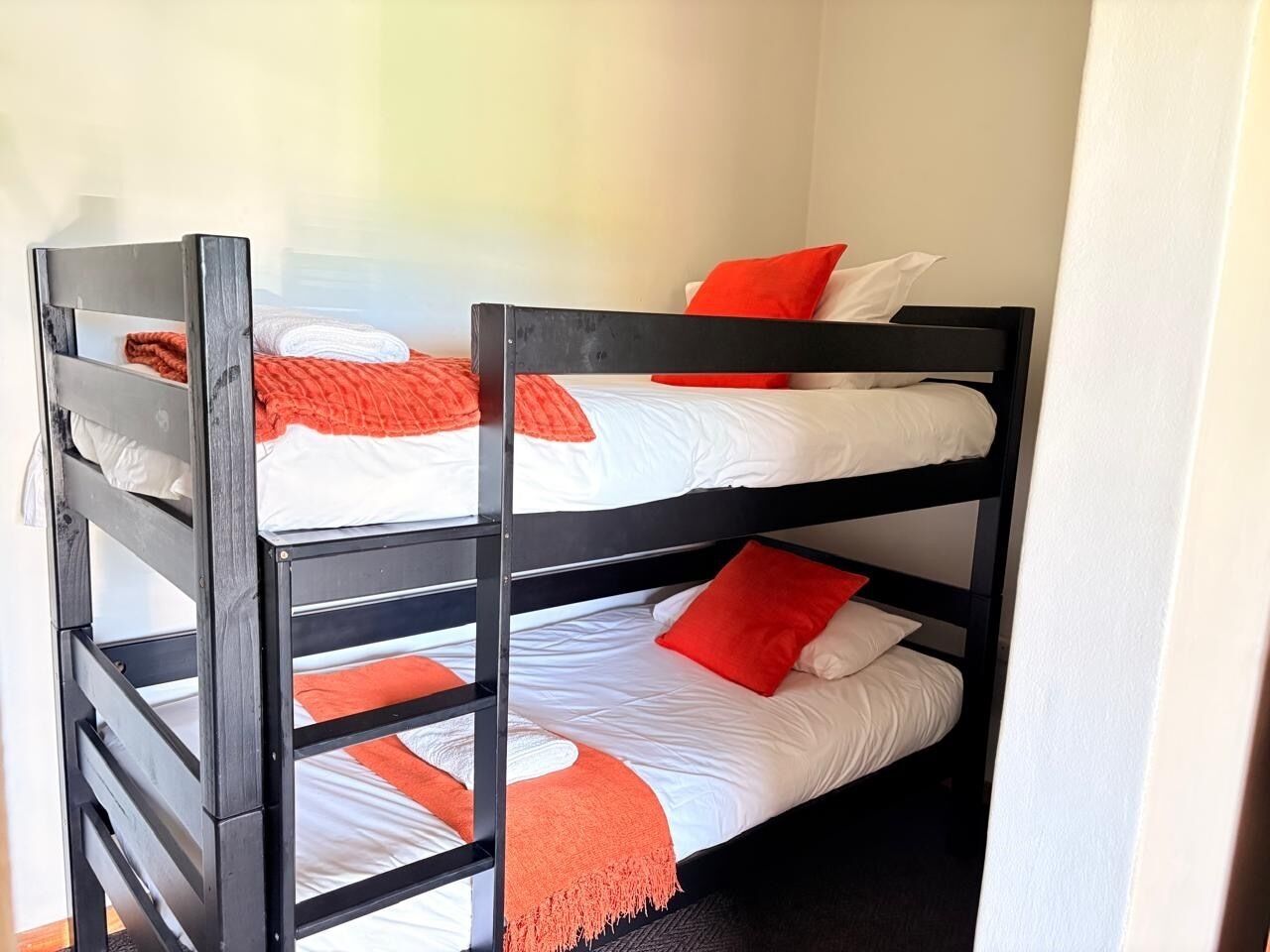 Una cama litera con tres niveles, cada uno con ropa de cama blanca y detalles anaranjados.