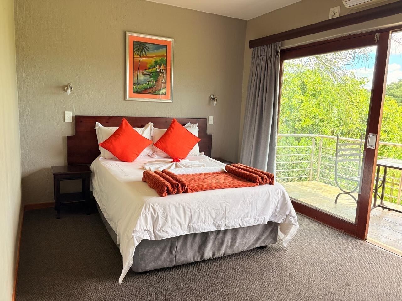 Une chambre d’hôtel avec un lit, un tableau, une fenêtre donnant sur un paysage et un balcon.