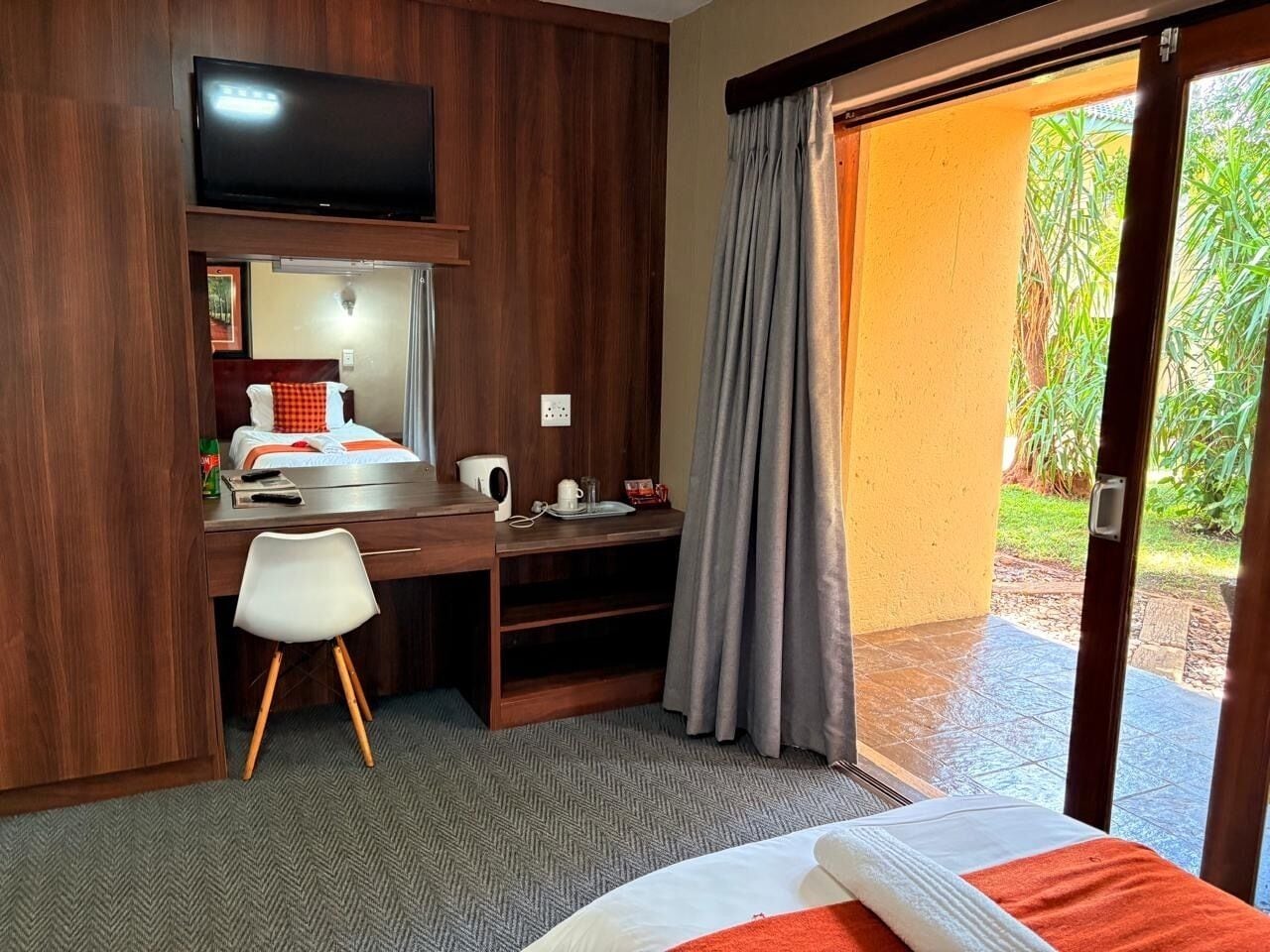 A hotel room with a bed, a desk with a chair, a television, and a view of the outdoors.